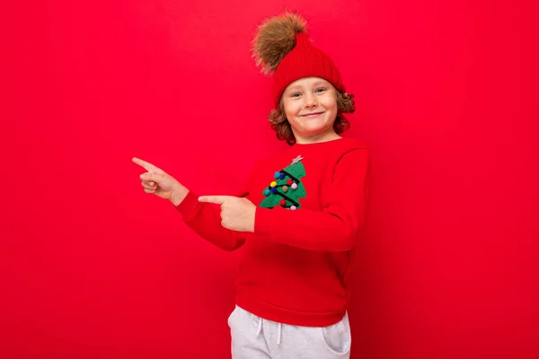 Cool pojke med lockar på en röd bakgrund i en tröja med en julgran — Stockfoto