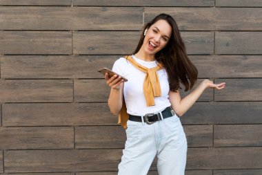 Kahverengi arka planda yalnız poz veren genç kadın, stüdyo portresi. İnsanların yaşam tarzı konsepti. Kopyalama alanı oluşturun. Cep telefonu kullanmak, SMS iletisi yazmak