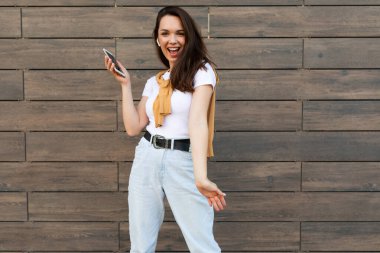 Kahverengi arka planda yalnız poz veren genç kadın, stüdyo portresi. İnsanların yaşam tarzı konsepti. Kopyalama alanı oluşturun. Cep telefonu kullanmak, SMS iletisi yazmak