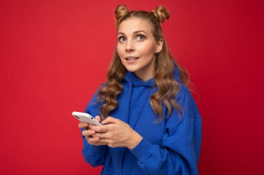 Düşünen genç ve güzel bir kadının görüntüsü. Kırmızı duvar arkasında cep telefonu kullanarak izole edilmiş poz veriyor..
