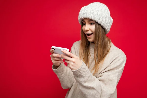 빨간 벽에 고립되어 있는 젊고 아름다운 여성이 핸드폰으로 게임을 하는 모습이 담긴 충격적 인 사진. — 스톡 사진