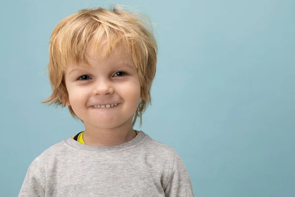 Ragazzo su sfondo blu, ritratto ravvicinato di un bambino con bei capelli e un sorriso malizioso — Foto Stock