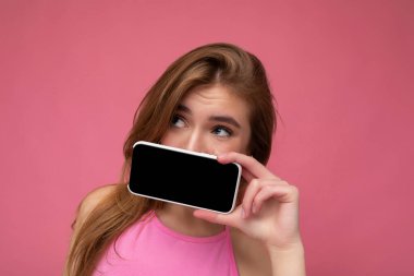 Pembe bluz giyen güzel sarışın bir kadının fotoğrafı. Pembe arka planda izole edilmiş. Elinde boş bir alan var.