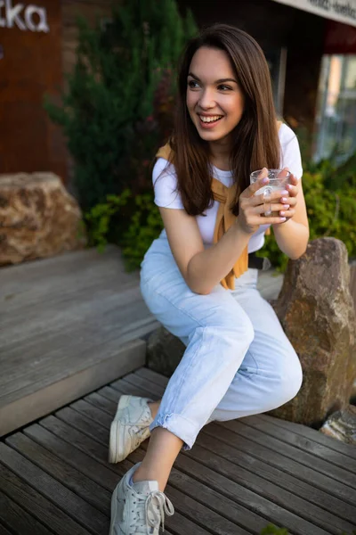 Roztomilý volný mladý žena těšit kávu, zatímco sedí v krásném letním parku na kameni — Stock fotografie