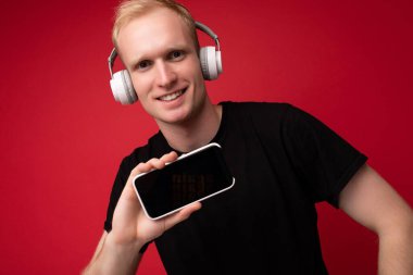 Yakışıklı, yakışıklı, yakışıklı, şık kıyafetler giyen, renkli arka plan duvarında tek başına duran, akıllı telefon tutan ve boş ekran ekranlı telefonu gösteren yakışıklı bir adam.