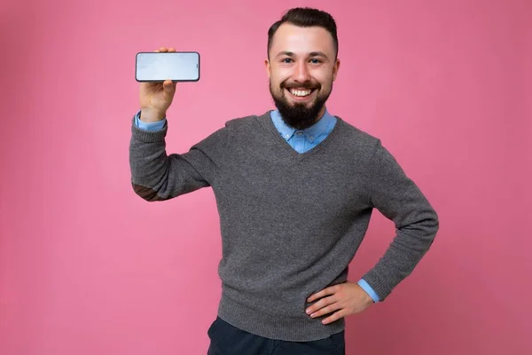 Bonito jovem legal feliz boa aparência vestindo roupas elegantes casuais de pé isolado sobre parede de fundo colorido segurando smartphone e mostrando telefone com tela vazia olhando — Fotografia de Stock