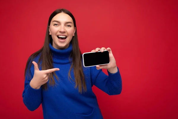 Photo of beautiful smiling young woman good looking wearing casual stylish outfit standing isolated on background with copy space holding smartphone showing phone in hand with empty screen display for — Stock Photo, Image