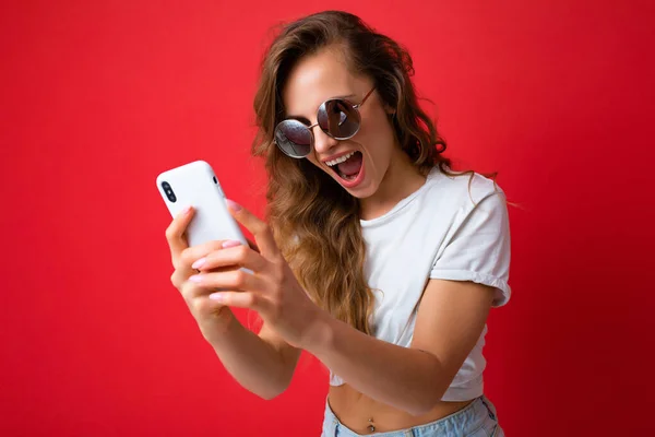 Attractive charming young smiling happy woman holding and using mobile phone taking selfie wearing stylish clothes isolated over wall background — Stock Photo, Image
