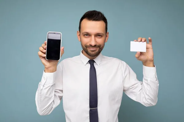 Hermoso joven guapo feliz guapo usando ropa elegante casual de pie aislado sobre la pared de fondo colorido sosteniendo el teléfono inteligente y mostrando el teléfono con pantalla vacía mirando —  Fotos de Stock