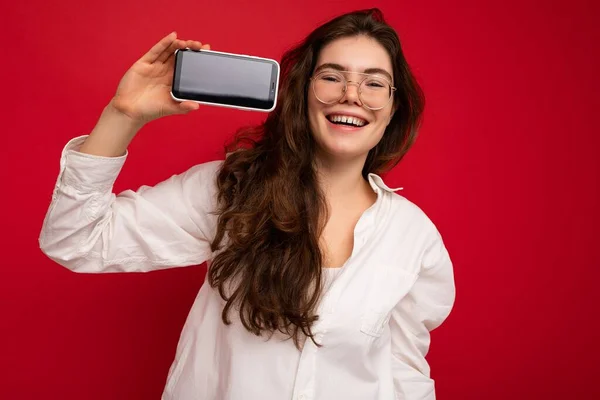 아름다운 미소를 가진 젊은 여성 이 평범 한 스타일의 복장을 한 채빈 화면을 보여 주는 스마트폰을 손에 들고 복사본 공간에 고립된 채서 있는 아름다운 사진 — 스톡 사진