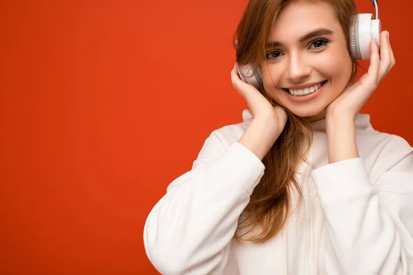 Closeup photo of attractive positive smiling young blonde female person wearing white hoodie isolated over colourful background wall wearing wireless headphones listening to good music and enjoying — Stock Photo, Image