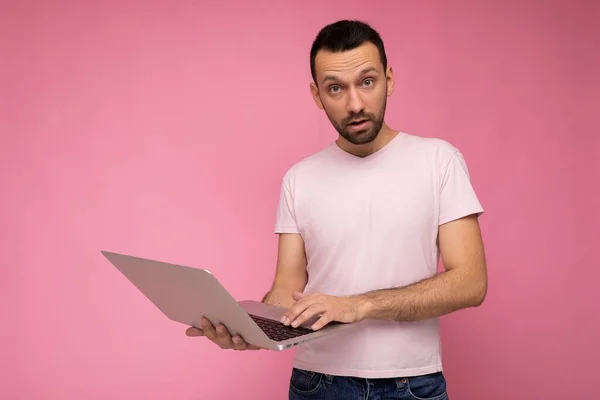 핑크 색 배경으로 티셔츠를 입고 카메라를 보고 있는 손님 이 컴퓨터를 들고 놀란 남자 — 스톡 사진