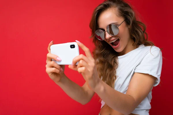 Foto close-up de incrível bela jovem loira mulher segurando telefone celular tirando foto selfie usando câmera de smartphone usando óculos de sol roupa elegante todos os dias isolado sobre parede colorida — Fotografia de Stock