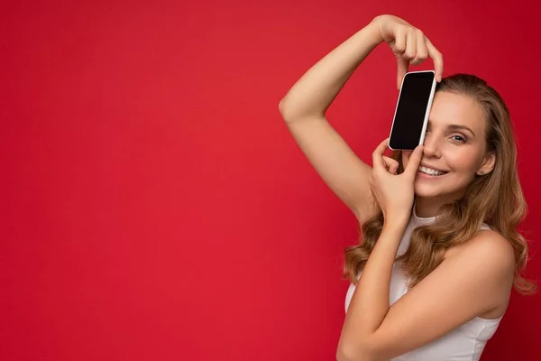 Photo of beautiful smiling young woman good looking wearing casual stylish outfit standing isolated on background with copy space holding smartphone showing phone in hand with empty screen display for — Stock Photo, Image