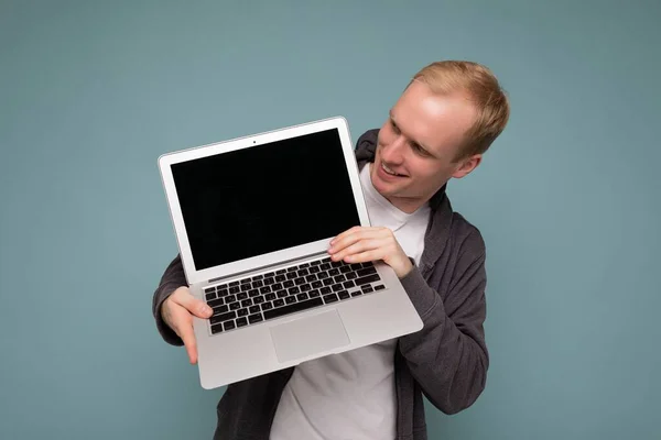 Retrato de primer plano del guapo hombre rubio sosteniendo la computadora portátil mirando hacia abajo en el teclado netbook usando ropa casual aislada sobre fondo azul —  Fotos de Stock