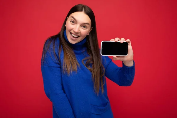 Photo of beautiful smiling young woman good looking wearing casual stylish outfit standing isolated on background with copy space holding smartphone showing phone in hand with empty screen display for — Stock Photo, Image