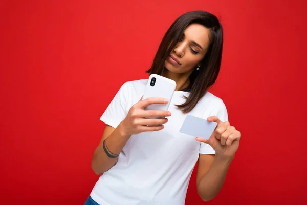 Pretty woman wearing everyday stylish clothes isolated on background wall holding and using phone and credit card making payment looking at smartphone screen — Stock Photo, Image