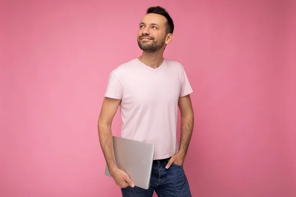 털이 없는 행복하고 마음씨좋은 젊은 청년이 고립 된 핑크 배경에 티셔츠를 입고 노트북 컴퓨터를 들고 올려다 보고 있습니다. — 스톡 사진