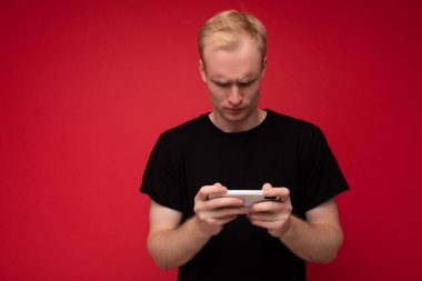 Yakından çekilmiş bir fotoğraf. Tatmin olmamış, mutsuz, üzgün, hoş görünümlü, şık giyinmiş, arka planda izole edilmiş, boş bir alanda saklanan ve cep telefonu kullanan genç bir adam.