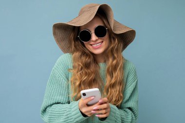 Gündelik kıyafetler giyen güzel genç bir kadın arka planda izole bir şekilde duruyor telefonla internette geziniyor ve mobil ekrana bakıyor.