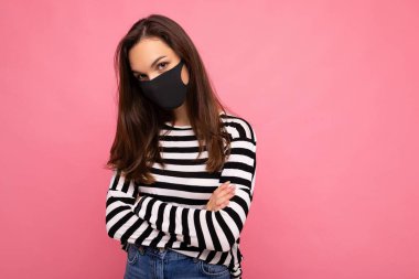 Yeniden kullanılabilir virüs koruyucu maskeli genç bir kadın pembe arka plan duvarında izole edilmiş koronavirüse karşı.