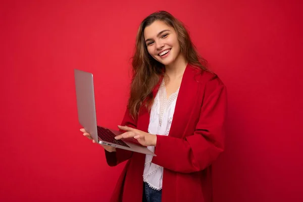 Side profile photo of charming smiling confident pretty young lady holding laptop wearing red cardigan and white t-shirt isolated on red wall background. — Stock Photo, Image