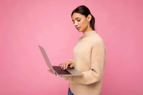 Profil lateral fotografie de fermecătoare doamnă destul de tânără care deține laptop izolat peste fundal de perete uitându-se la netbook tastarea pe textul tastaturii și gândindu-se la ceva — Fotografie, imagine de stoc