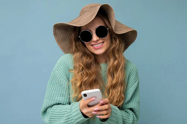 Piękna młoda kobieta w luźnych ubraniach stojąca samotnie nad tłem surfując w Internecie przez telefon patrząc na ekran mobilny — Zdjęcie stockowe