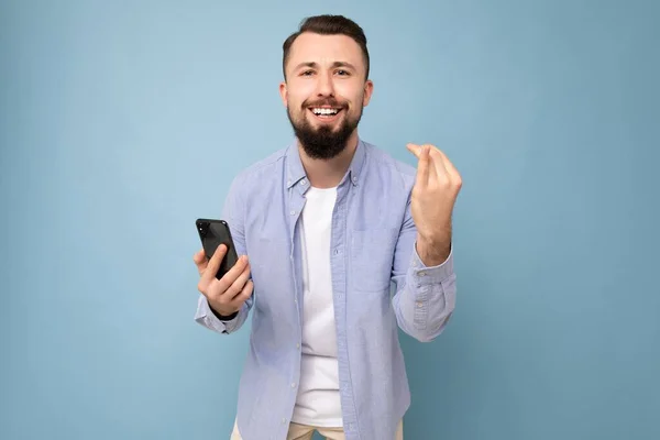 하얀 티셔츠와 파란 셔츠를 입고 빈 공간을 손에 쥐고 전화 메시지를 보며 푸른 배경에 고립 된 행복 한 젊고 잘생긴 브라 운트 벗은 남자 — 스톡 사진