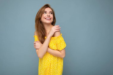 Çekici, mutlu, günlük kıyafetler giyen, renkli arka planda tek başına duran, yan tarafa bakan genç bir kadın.