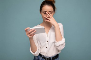 Oldukça üzgün, genç, sarışın kıvırcık kadın. Gözleri kapalı, günlük beyaz gömlek giyiyor. Mavi arka plan duvarında izole edilmiş.