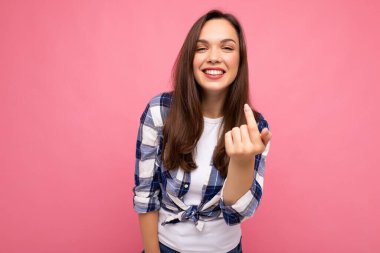 Mutlu, gülümseyen, samimi duyguları olan, modaya uygun bir çek tişörtü giyen, pembe arka planda boş alan olan güzel esmer kadın.