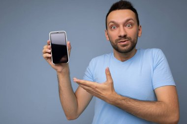 Yakışıklı, yakışıklı, yakışıklı, şık kıyafetler giyen, renkli arka plan duvarında tek başına duran, akıllı telefon tutan ve boş ekran ekranlı telefonu gösteren yakışıklı bir adam.