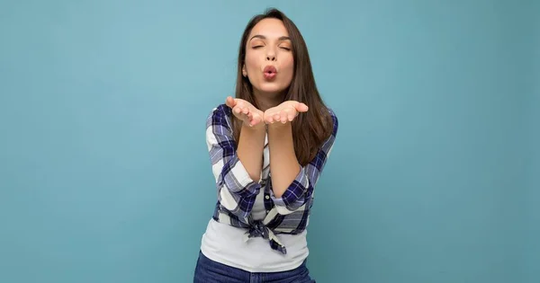 Panoramic portrait of young positive happy beautiful winsom brunette woman with sincere emotions wearing check shirt poising isolated over blue background with copy space and giving kiss — Stock Photo, Image