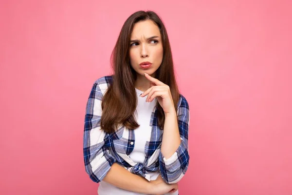 Shot of young thinking beautiful brunette woman with sincere emotions wearing trendy check shirt isolated on pink background with empty space and having doubts — Stock Photo, Image