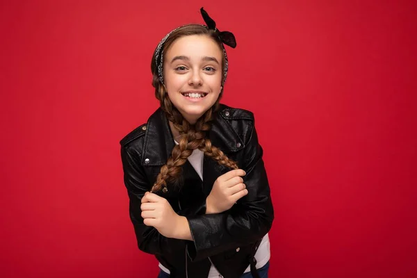 Primer plano de foto de la hermosa niña morena sonriente feliz con coletas con chaqueta de cuero negro de moda y camiseta blanca de pie aislado sobre la pared de fondo rojo mirando a la cámara — Foto de Stock