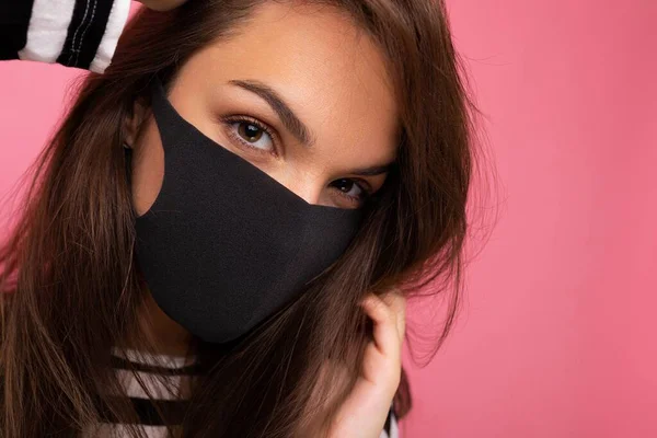 Foto de primer plano de la joven hermosa mujer en la máscara protectora del virus reutilizable en la cara contra el coronavirus aislado en la pared de fondo rosa — Foto de Stock