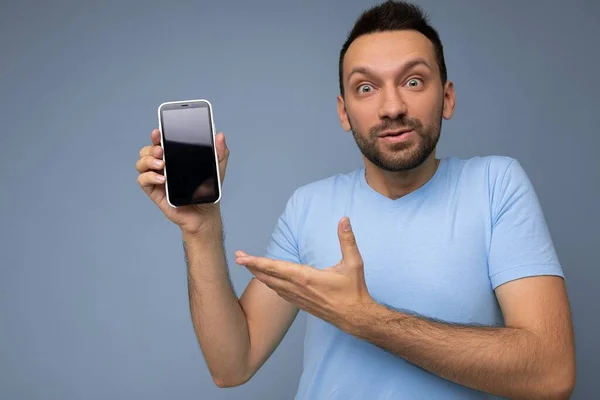 Schöner glücklicher cooler junger Mann gut aussehend in lässiger stylischer Kleidung, isoliert vor bunter Hintergrundwand stehend, Smartphone haltend und Handy mit leerem Bildschirm anschauend — Stockfoto