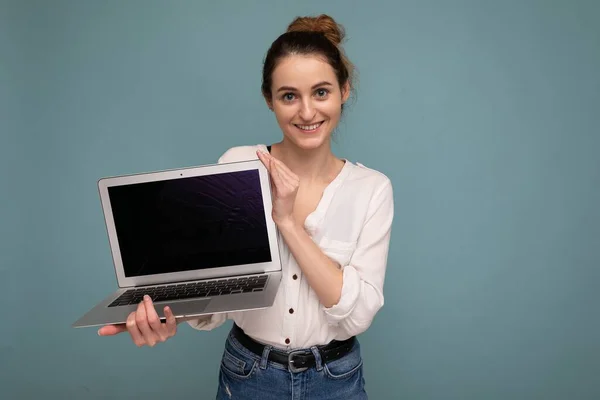 Frumos zâmbind tânără femeie care deține netbook computer uitându-se la camera foto purtând cămașă albă izolată pe fundal albastru — Fotografie, imagine de stoc
