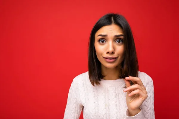 Retrato de hermosa triste triste triste joven morena con jersey de punto aislado sobre fondo rojo con espacio de copia y tocando el pelo castaño corto y tener puntas abiertas — Foto de Stock