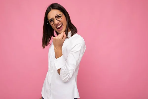 Jonge positieve koele mooie brunet vrouw met wit shirt en optische bril geïsoleerd over roze achtergrond met lege ruimte en met rock 'n roll gebaar — Stockfoto