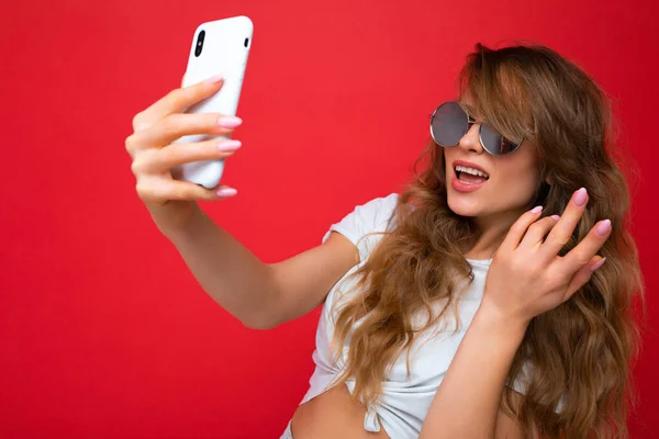 Atraente encantador jovem sorrindo feliz mulher segurando e usando telefone celular levando selfie vestindo roupas elegantes isolado sobre fundo da parede — Fotografia de Stock