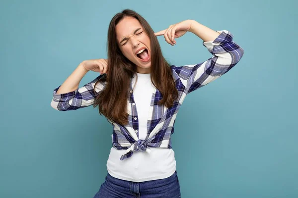 Mladý emocionální atraktivní brunetka žena izolované na modrém pozadí s kopírovacím prostorem a zakrývající uši a křik — Stock fotografie