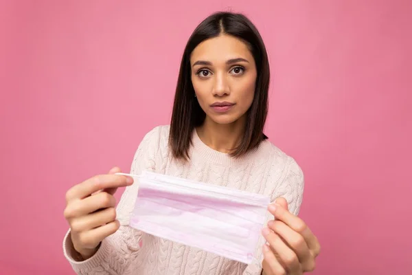 Brunett kvinna som håller en antivirusskydd mask för att förhindra andra från corona COVID-19 och SARS cov 2 infektion isolerad på rosa bakgrund — Stockfoto