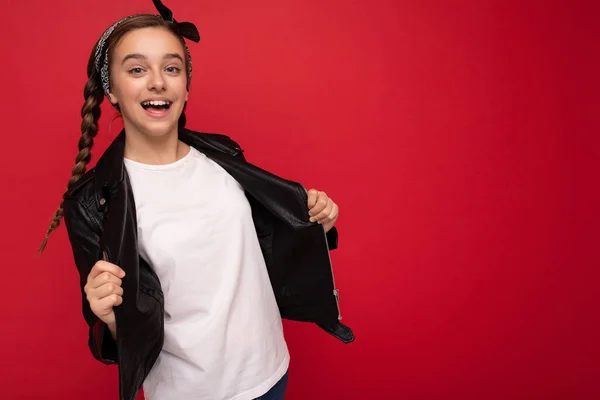 Photo of beautiful happy smiling brunette girl with pigtails wearing stylish black leather jacket and white t-shirt for mockup isolated over red background looking at camera