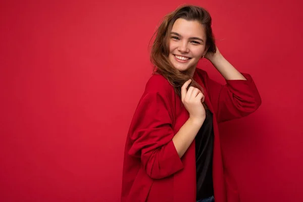 Портрет позитивной веселой модной женщины в формальной одежде, смотрящей на камеру на красном фоне с копировальным пространством — стоковое фото
