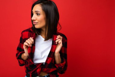 Genç, pozitif pozitif, havalı, seksi, samimi duyguları olan, beyaz tişört giyen esmer kadın ve kırmızı arka planda izole edilmiş, özgür bir kırmızı çek tişörtü.