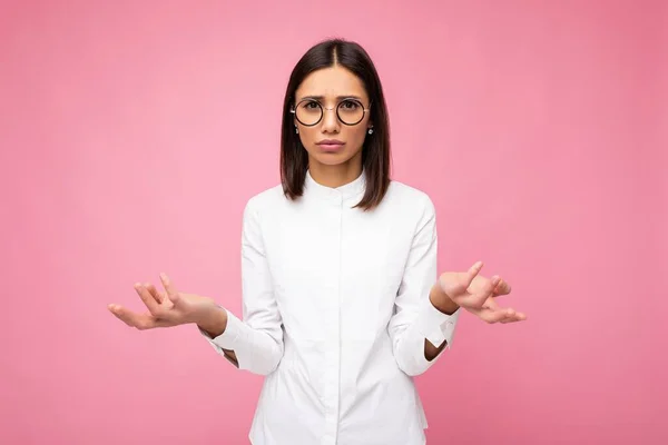 Atractiva preguntando mujer morena joven insatisfecha usando ropa elegante todos los días y gafas ópticas modernas aisladas en la pared de fondo colorido mirando a la cámara y teniendo dudas — Foto de Stock