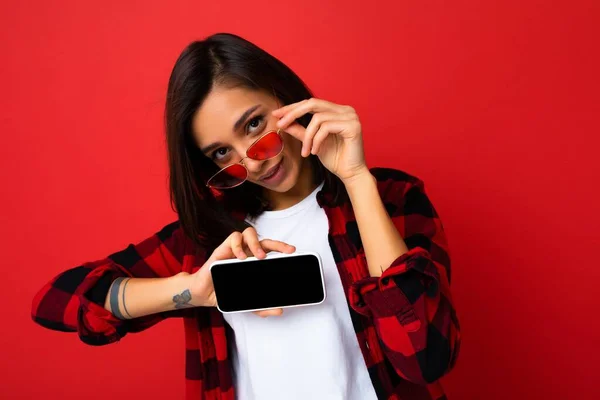 Fénykép a szexi gyönyörű mosolygós fiatal nő jóképű visel alkalmi elegáns ruhát áll elszigetelt a háttérben másolás tér gazdaság okostelefon mutatja a telefont a kezében üres képernyőn — Stock Fotó
