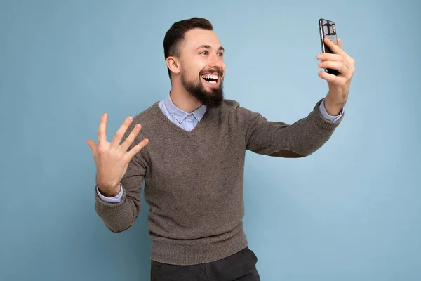 Side-profile Photo of positive handsome young brunette unshaven man with beard wearing casual grey sweater and blue shirt isolated on pink background wall holding smartphone having video call looking — Stock Photo, Image
